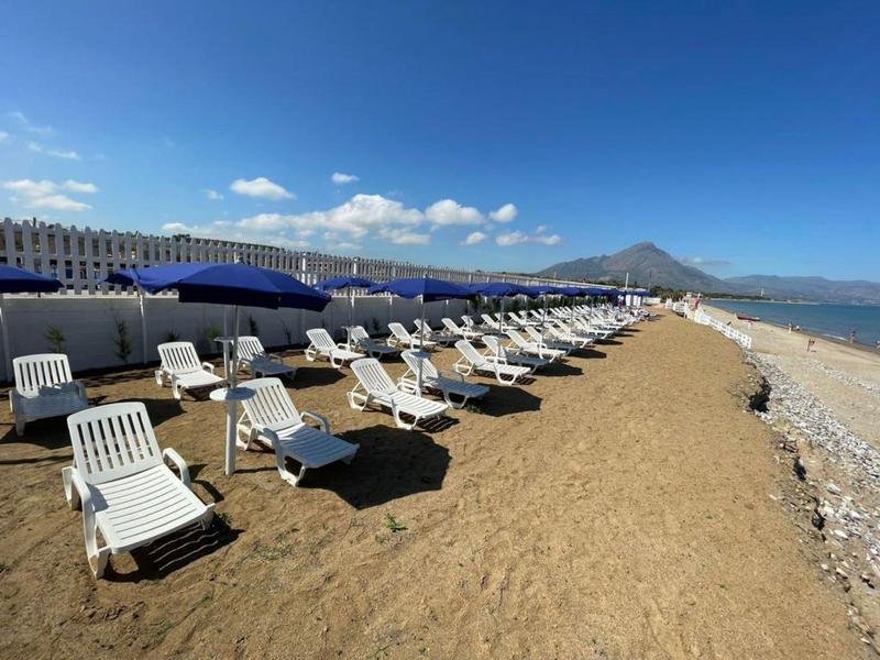 Empty lounge chairs in rows on sandy beach in front of a hotel with mountain view