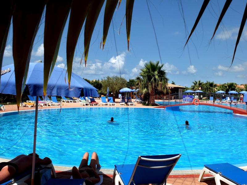 Large pool area with blue lounge chairs and umbrellas under a clear sky.