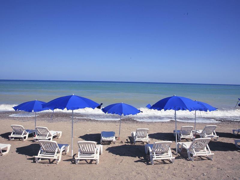 Beach with white loungers and blue umbrellas by calm sea under clear blue sky