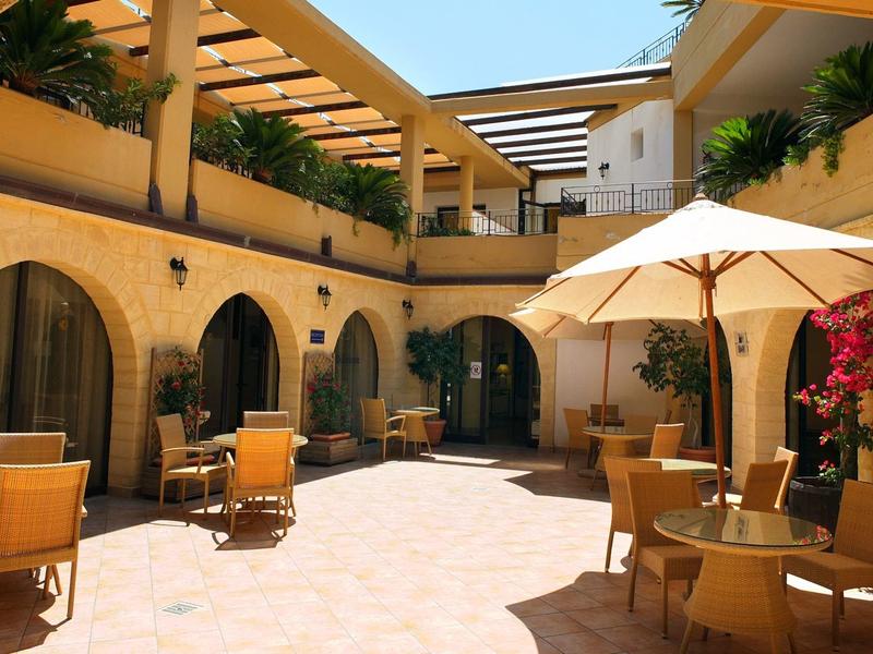 Hotel courtyard with tables, chairs, and umbrellas in warm yellow lighting.