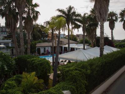 Blick auf entspannten Poolbereich mit Palmen und Sonnenliegen im Hotelgarten bei Sonnenuntergang.