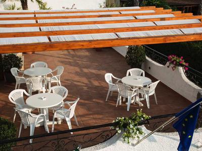 Freiluft-Terrasse mit runden weißen Tischen, Stühlen, Holzlamellen und Blumenarrangements.