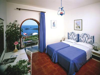 Camera luminosa con due letti singoli, decorazioni blu e vista sul mare attraverso finestra ad arco.