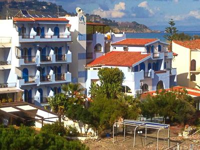 Hotel su più piani con facciata bianca e tetti rossi in una zona costiera soleggiata.