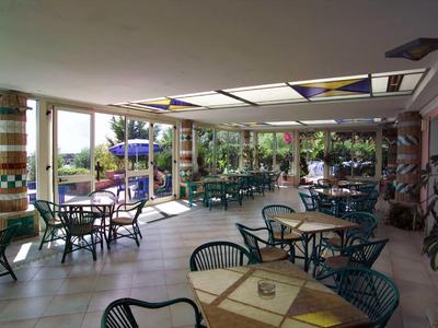 Überdachte Terrasse mit Tischen und Stühlen in einem Hotel, mit Blick auf den Pool und Garten.