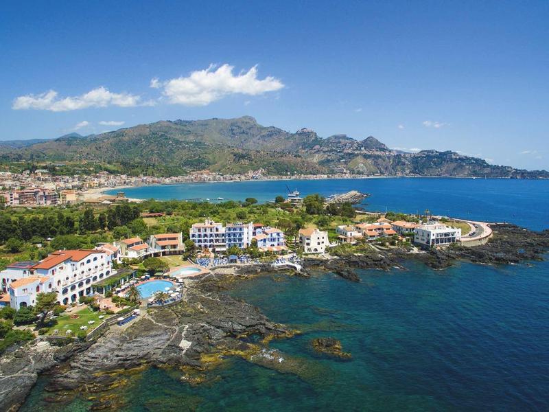 Paesaggio con edifici di hotel sulla costa rocciosa e montagne sullo sfondo sotto un cielo limpido.