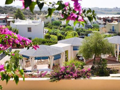 Vue d'un complexe hôtelier calme avec des plantes en fleurs et des pavillons sous un ciel clair.