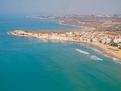Ligne côtière avec plage, mer calme et bâtiments le long du rivage sous un ciel clair.