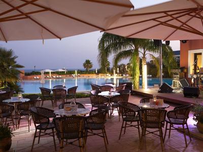 Terrasse du soir avec tables et chaises à côté d'une piscine éclairée et de palmiers.
