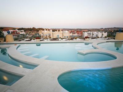 Piscine ronde à plusieurs niveaux avec sièges, vue sur des bâtiments résidentiels au coucher du soleil.