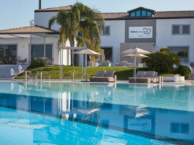 Großes weißes Haus mit Palmen und blauen Pool, Sonnenschirmen und Liegestühlen im Garten.