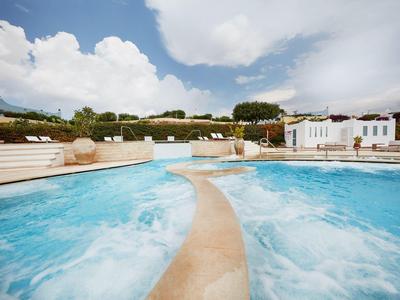 Grand jacuzzi extérieur avec eau bleue bouillonnante et bâtiment blanc en arrière-plan.
