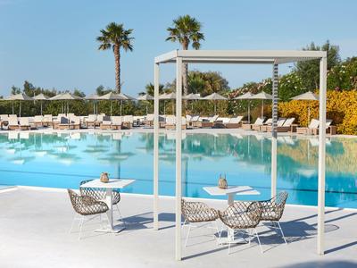 Espace piscine moderne avec fauteuils suspendus, palmiers et nombreuses chaises longues sous des parasols blancs.