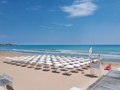 Plage avec des rangées de parasols blancs et un voilier sur la mer bleue calme.