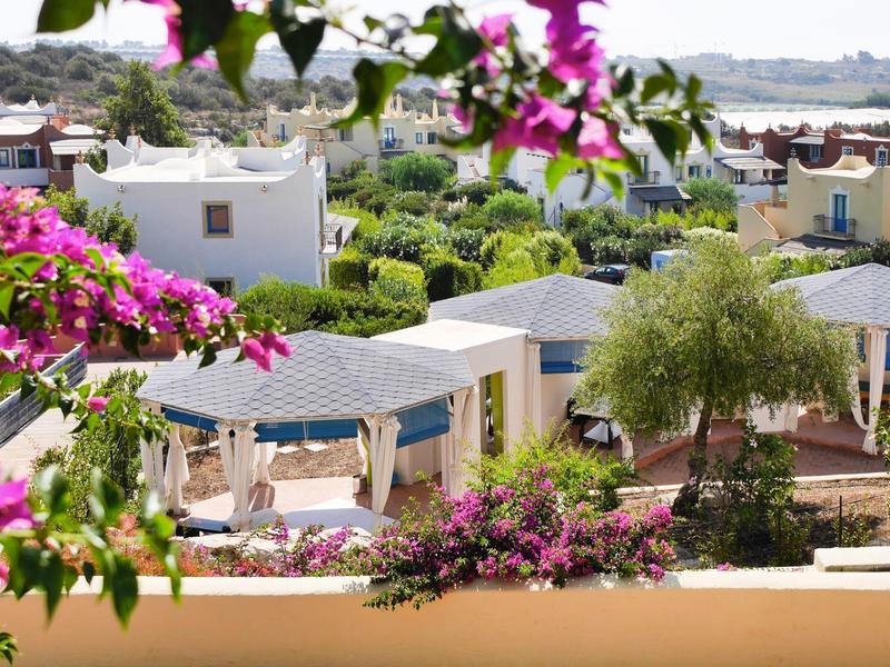 Vue d'un complexe hôtelier calme avec des plantes en fleurs et des pavillons sous un ciel clair.