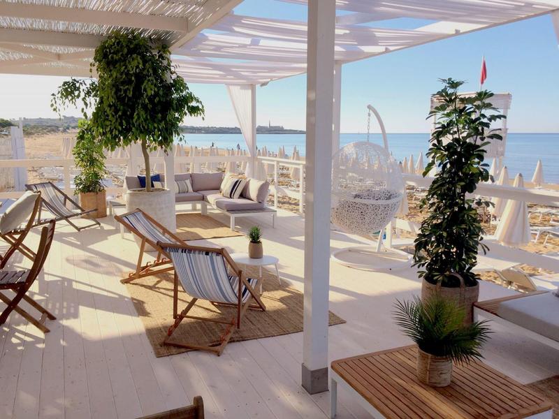 Salon de plage lumineux avec chaises longues blanches sous un pavillon ouvert avec vue sur la mer.