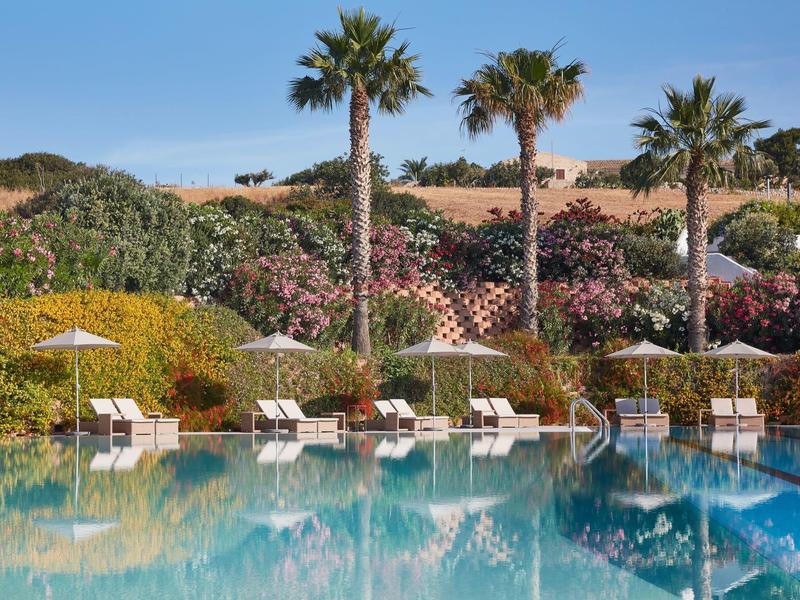 Eau claire et bleue de la piscine d'hôtel avec des palmiers et des chaises longues blanches en arrière-plan.