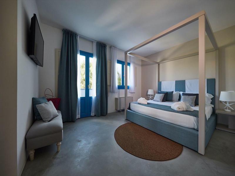 Chambre d'hôtel lumineuse avec lit à baldaquin, fauteuil gris, tapis et téléviseur à écran plat mural.