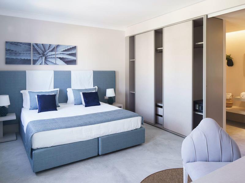 Chambre d'hôtel moderne avec lit double, tables de chevet, art mural abstrait et dressing.