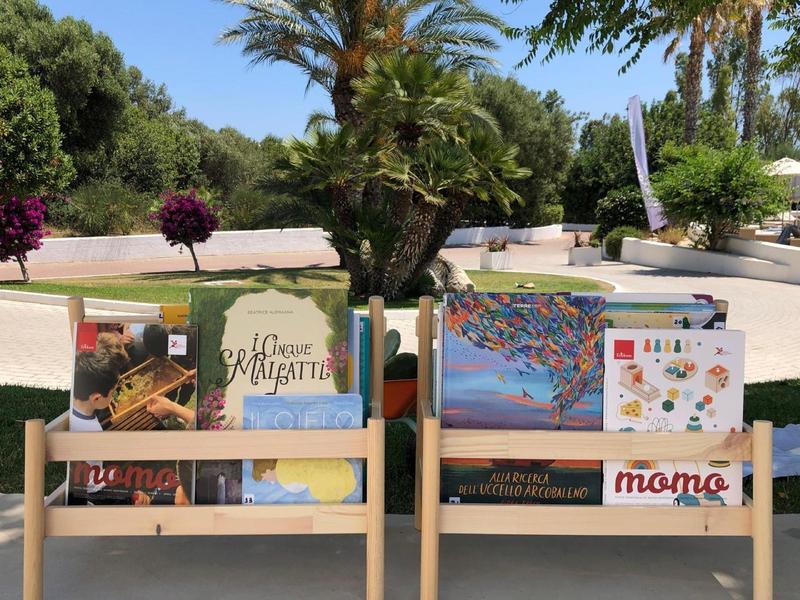Présentoir avec cartes postales et livres d'art en plein air à côté des palmiers.
