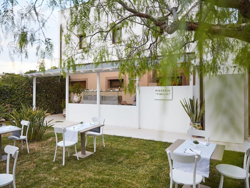 Coin extérieur convivial avec tables et chaises blanches sur pelouse verte devant un bâtiment moderne.