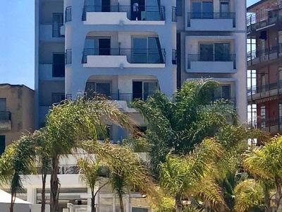 Bâtiment d'hôtel à plusieurs étages avec balcons et palmiers au premier plan sous un ciel dégagé.