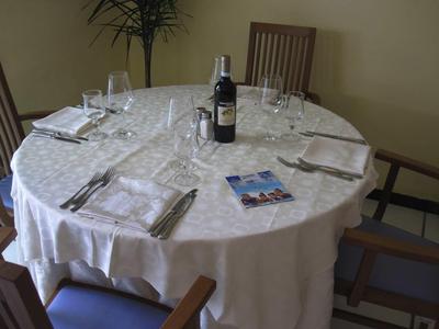 Table ronde dressée avec nappe blanche, verre à vin, bouteille de vin et couverts dans une salle à manger.