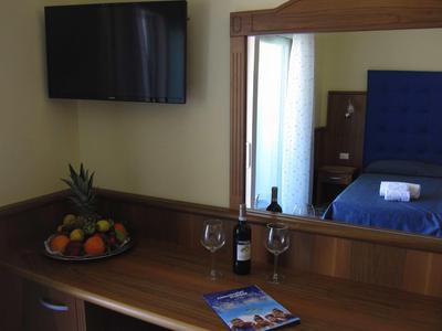 Chambre d'hôtel avec télévision, miroir, lit, bouteille de vin, verres à vin et plateau de fruits.
