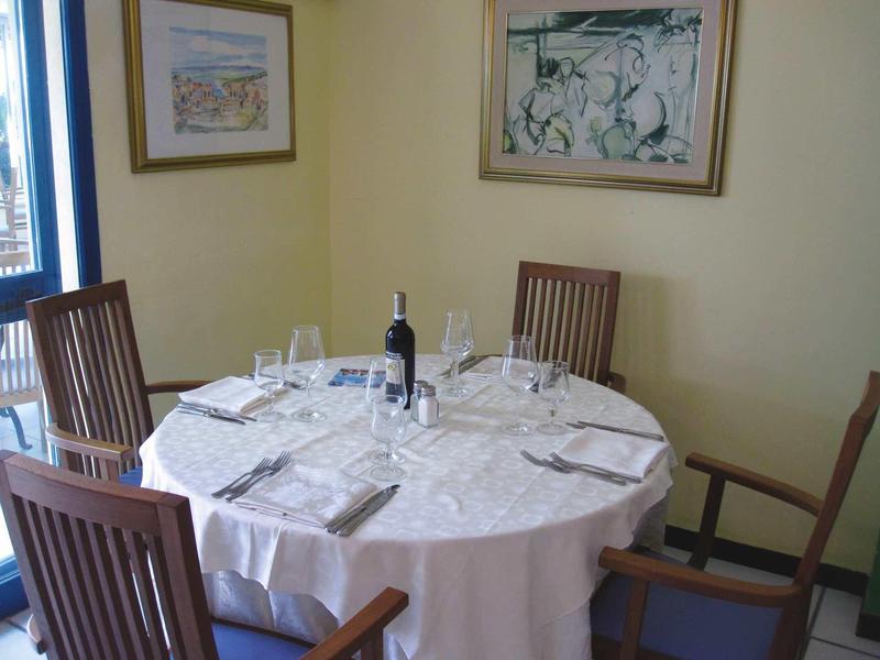 Table ronde avec nappe blanche, bouteille de vin, verres et couverts dans une salle à manger lumineuse.