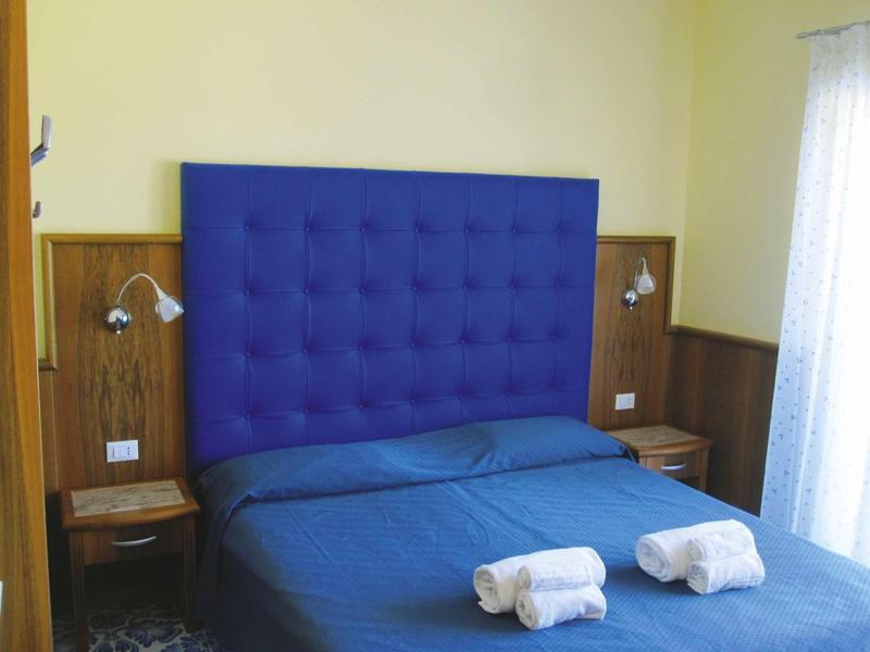 Chambre moderne avec tête de lit bleue, lit double et deux serviettes blanches roulées.
