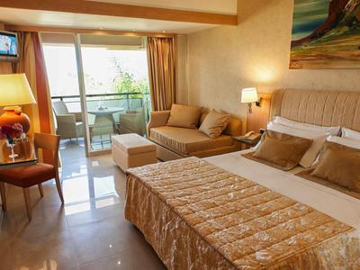 Chambre d'hôtel confortable avec lit double, canapé, bureau et balcon avec vue sur la mer.