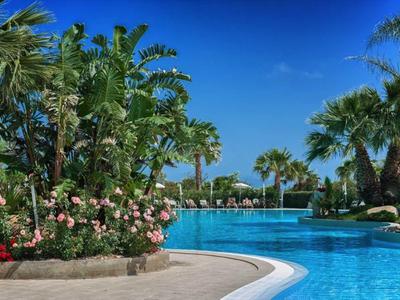 Une piscine bleue claire entourée de palmiers luxuriants et de plantes en fleurs sous un ciel clair.
