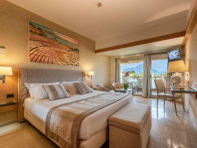 Modern eingerichtetes Hotelzimmer mit großem Doppelbett und Balkon mit Meerblick.