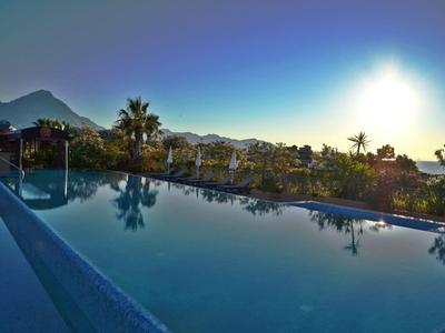 Infinity-Pool mit Palmen und Bergen im Hintergrund bei Sonnenuntergang.