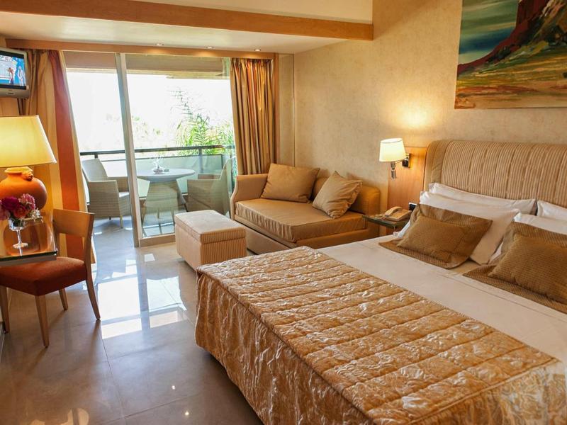 Chambre d'hôtel confortable avec lit double, canapé, bureau et balcon avec vue sur la mer.