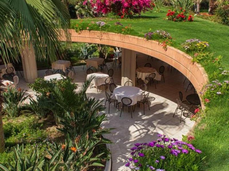 Terrasse d'hôtel avec des tables entourées d'une végétation tropicale luxuriante et de plantes en fleurs.