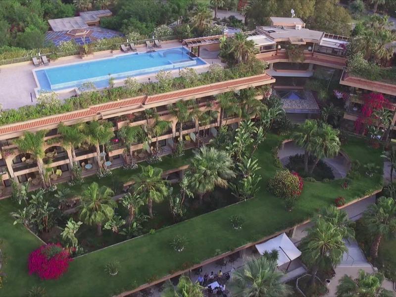 Vue aérienne d'un hôtel avec une piscine sur le toit et un environnement verdoyant.