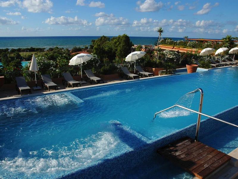 Piscine d'hôtel avec jacuzzi, chaises longues et vue sur la mer sous ciel bleu
