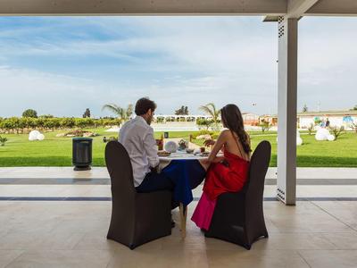 Pareja sentada al aire libre en una mesa puesta con vistas a un césped verde y cielo despejado.