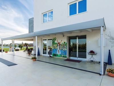 Modernes weißes Haus mit großer überdachter Terrasse und Glasfenstern, blauer Himmel im Hintergrund.