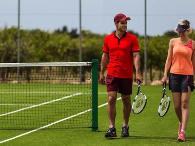 Un hombre y una mujer caminan con raquetas de tenis en una cancha de césped.