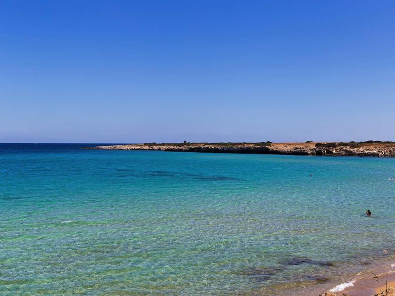 Čisté modré moře s štěrkovou pláží a vzdáleným pobřežím pod bezmračnou oblohou