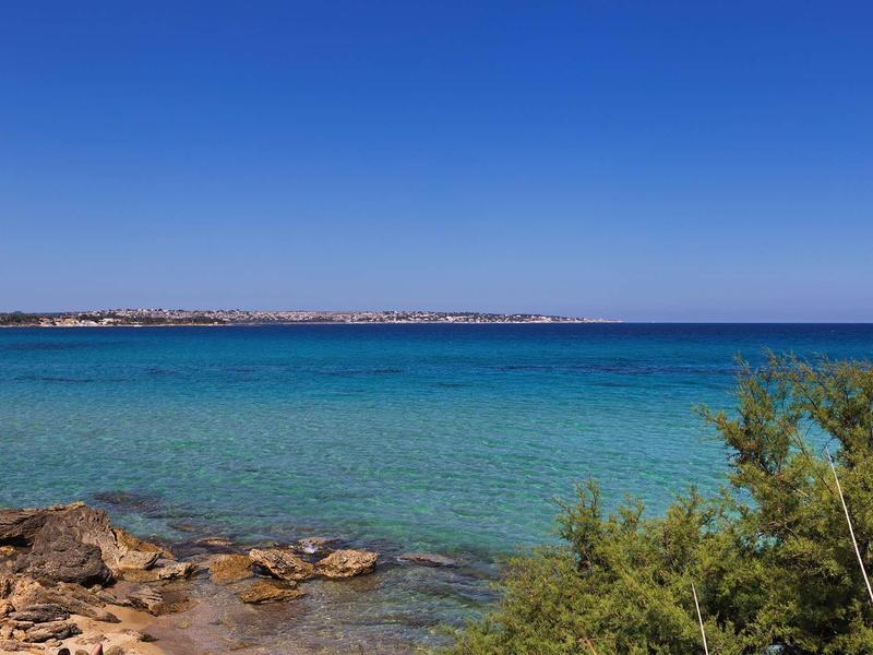 Čisté modré moře s skalnatým pobřežím a zeleným keřem pod bezmračnou oblohou