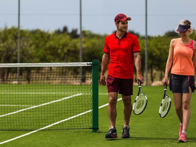 Dvě osoby jdoucí vedle sebe na tenisovém dvorci s tenisovými raketami.