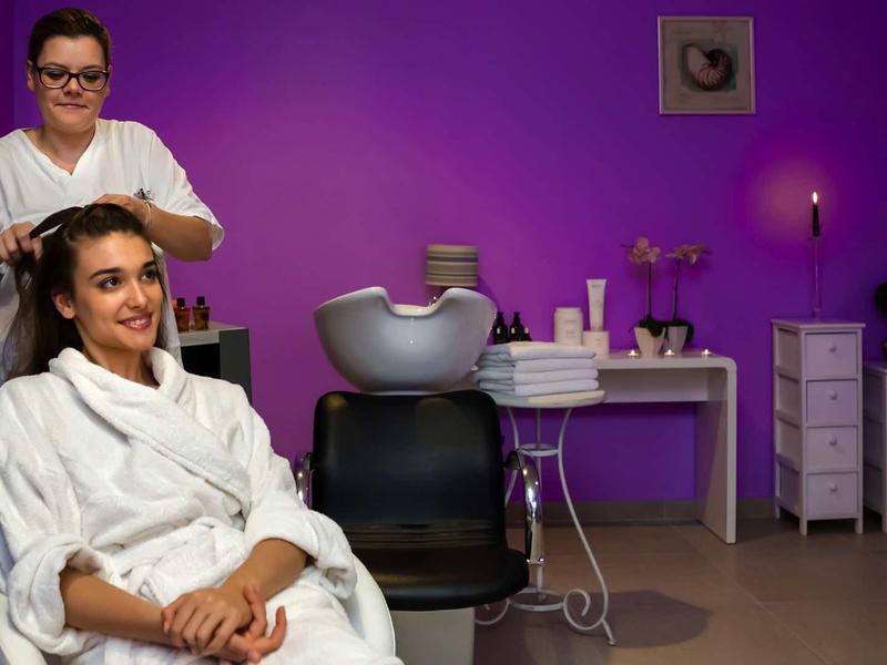 Žena dostává vlasovou kúru v moderním wellness s fialovými zdmi.