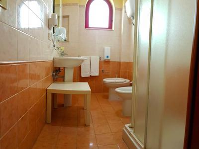 Small bathroom with sink, toilet, shower, and window with semicircular frame.