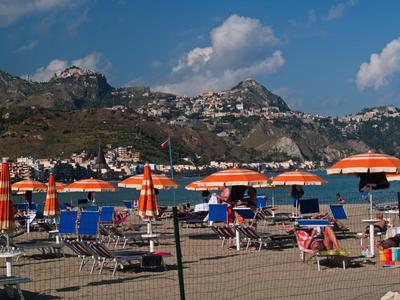 Beach with orange umbrellas and loungers in front of a mountainous backdrop under a blue sky.