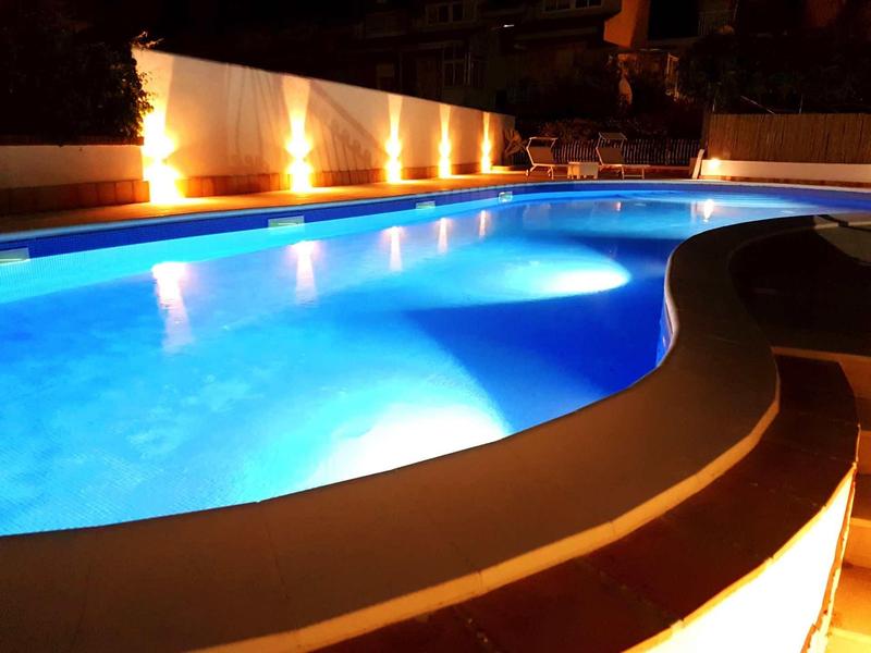 Illuminated outdoor pool with curved shape and seating area at night.