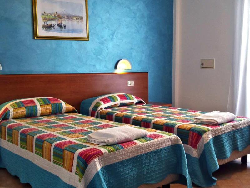 Room with two single beds, colorful blankets, and blue accent wall.