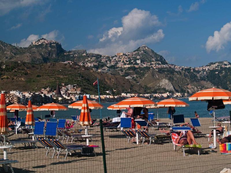 Beach with chairs and orange-white umbrellas in front of mountains and blue sky.